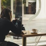 A woman enjoys coffee while using her smartphone at a cozy cafe table.